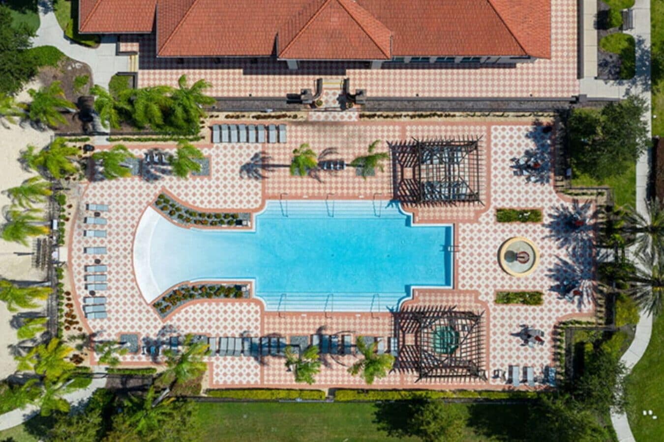 An aerial view of a resort with a central swimming pool, sun loungers, and palm trees.