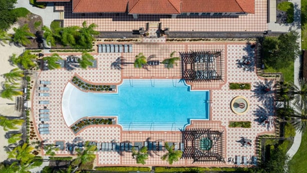 Vue aérienne d’un complexe hôtelier avec une piscine centrale, des chaises longues et des palmiers.