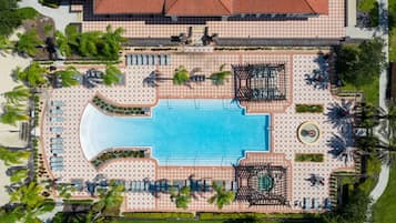 An aerial view of a resort with a central swimming pool, sun loungers, and palm trees.