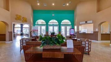 A spacious lobby with a central wooden table, comfortable seating, and large windows.