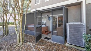 Un espacio de estar al aire libre techado con un jacuzzi, una puerta corrediza de vidrio que da a una cocina y un equipo de aire acondicionado.