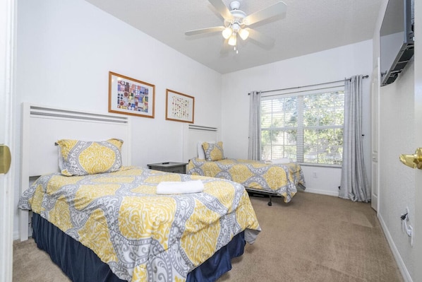 A hotel room with two beds, a ceiling fan, a window with curtains, and artwork on the wall.