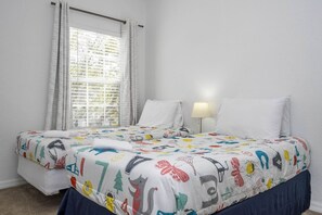 A bedroom with a bed, two pillows, a bedside lamp, and a window with curtains.