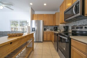 Une cuisine moderne dotée de meubles en bois, d’appareils électroménagers en acier inoxydable et d’un coin repas avec une table et un banc en bois.