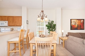 Une cuisine moderne avec des meubles en bois, une table à manger avec des chaises, un luminaire suspendu et un tableau au mur.