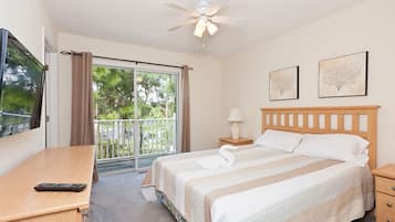 Habitación de hotel con cama, escritorio, silla, televisor, ventilador de techo, ventana con cortinas y dos cuadros en la pared.