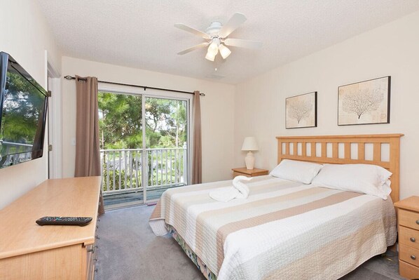 A hotel room with a bed, a desk, a chair, a TV, a ceiling fan, a window with curtains, and two framed pictures on the wall. - Emerald Island Townhome just 10min to Disney (Kissimmee)