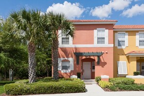 A two-story building with a red facade, white window shutters, and a number '8421' above the entrance. - Emerald Island Townhome just 10min to Disney (Kissimmee)