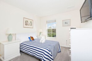 A bedroom with a bed, two bedside tables, a television, and a window. - Emerald Island Townhome just 10min to Disney (Kissimmee)