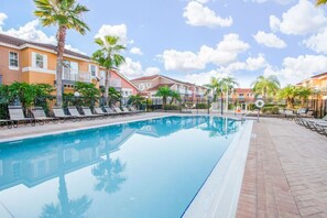 Una piscina con sillas de descanso, palmeras y una hilera de edificios al fondo.