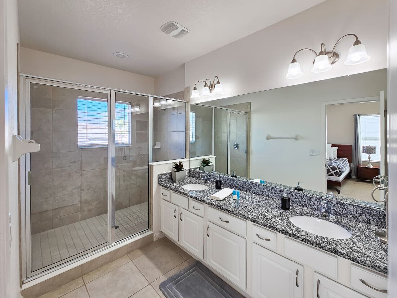 A modern bathroom with a glass-enclosed shower, dual sinks, and a large mirror.