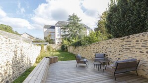 Une terrasse en bois avec des meubles d’extérieur, un mur en pierre et un bâtiment en arrière-plan.