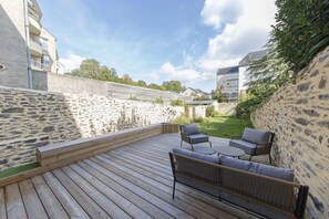A wooden deck with outdoor furniture, a stone wall, and buildings in the background.
