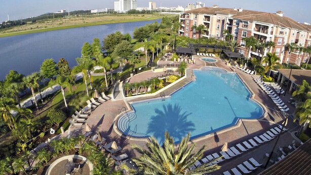 A hotel with a large swimming pool surrounded by lounge chairs and palm trees.