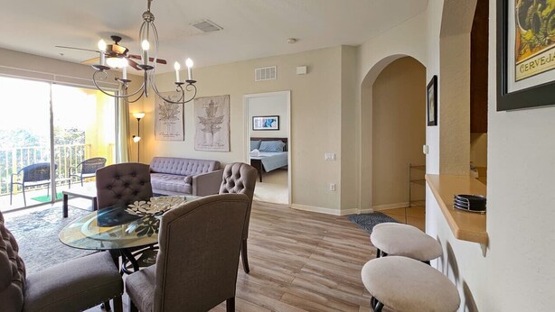A dining area with a glass table, cushioned chairs, and a chandelier. - Modern Condo  5min to Conv Center  with balcony (Orlando)