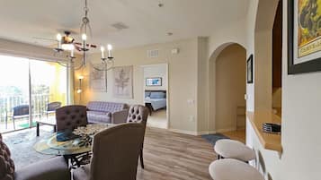 A dining area with a glass table, cushioned chairs, and a chandelier.
