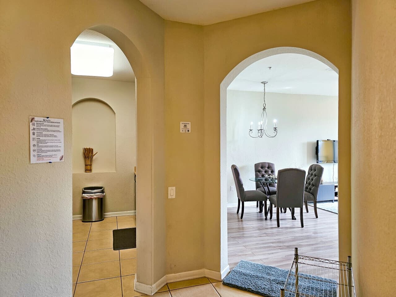 A hallway leading to a dining area with a chandelier, a trash can, and a sign on the wall.