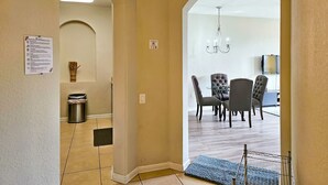 A hallway leading to a dining area with a chandelier, a trash can, and a sign on the wall. - Modern Condo  5min to Conv Center  with balcony (Orlando)