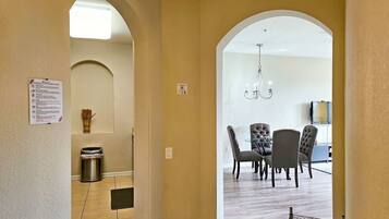 A hallway leading to a dining area with a chandelier, a trash can, and a sign on the wall.