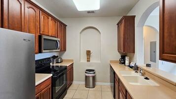 A modern kitchen with wooden cabinets, a stainless steel refrigerator, a microwave, and a sink.