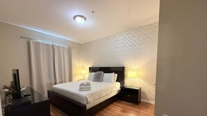 A modern bedroom with a bed, bedside tables, a TV, and a desk. - Spacious Condo 5min to Universal and Conv Center (Orlando)