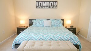 A bedroom with a bed, two bedside tables, a wall-mounted artwork, and an ottoman.