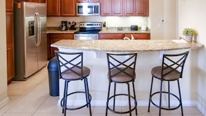 A kitchen with wooden cabinets, stainless steel appliances, a granite countertop, and three bar stools.