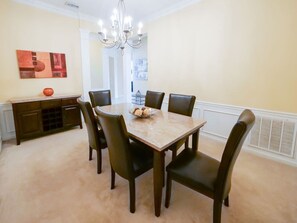 Un comedor con una mesa rectangular, seis sillas, una araña y un cuenco decorativo sobre la mesa.