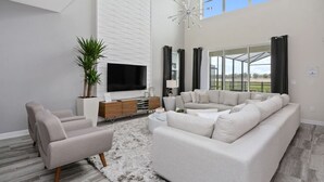 Un salon moderne avec un grand téléviseur à écran plat, un canapé d’angle blanc, une table basse et une plante en pot.