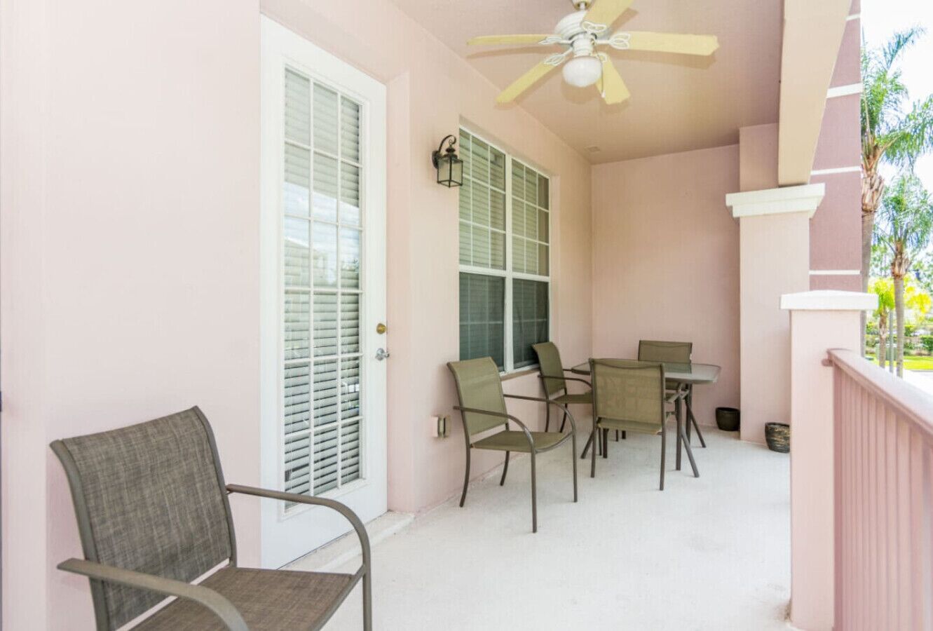 A balcony with a ceiling fan, a table with chairs, and a door with shutters.