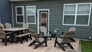 Een terras met een tafel, stoelen, een stenen bankje en een huis met een deur en ramen.