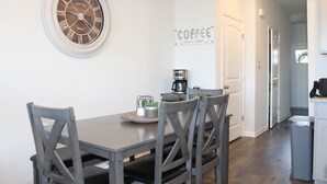 Een eetruimte met een ronde tafel, vier stoelen, een klok en een bord met opschrift 'koffie' aan de muur.