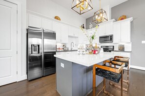 Cozinha moderna com armários brancos, eletrodomésticos de aço inoxidável e uma ilha central com banquetas.