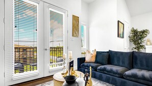 A living room with a dark blue sofa, a round coffee table with decorative items, and a view of a balcony with white blinds. - Spacious 3BR Houston Escape near Downtown with Spa (Houston)