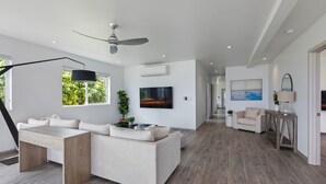 A modern living room with a sofa, a coffee table, a TV, and a ceiling fan. - The Makai Manor - Beautiful Newly Built Spacious Home (Honolulu)