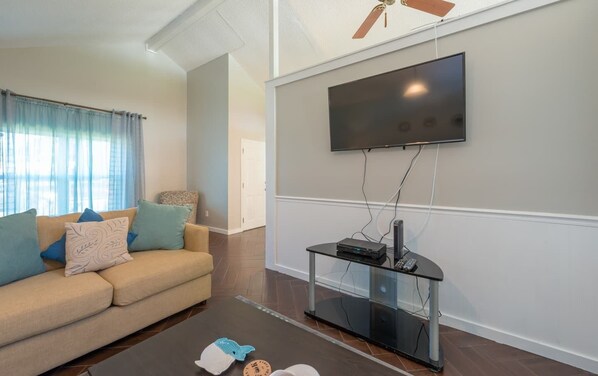 A living room with a sofa, TV, and a glass coffee table. - GATEWAY TO DISNEY AND FAMILY RETREAT CENTER (Deltona)