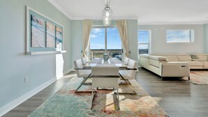 Una sala de estar moderna con comedor, un sofá color beige, un ventanal con cortinas y un candelabro.