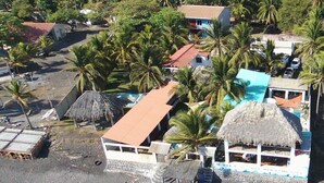 A coastal area with thatched-roof buildings, palm trees, and a beach. - Aqua Vista Beach House (Sonsonate)