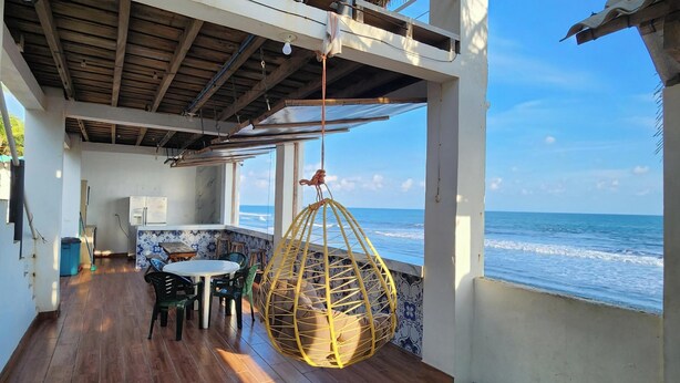 A covered patio with a wooden table and chairs, a hanging chair, and a view of the ocean. - Aqua Vista Beach House (Sonsonate)