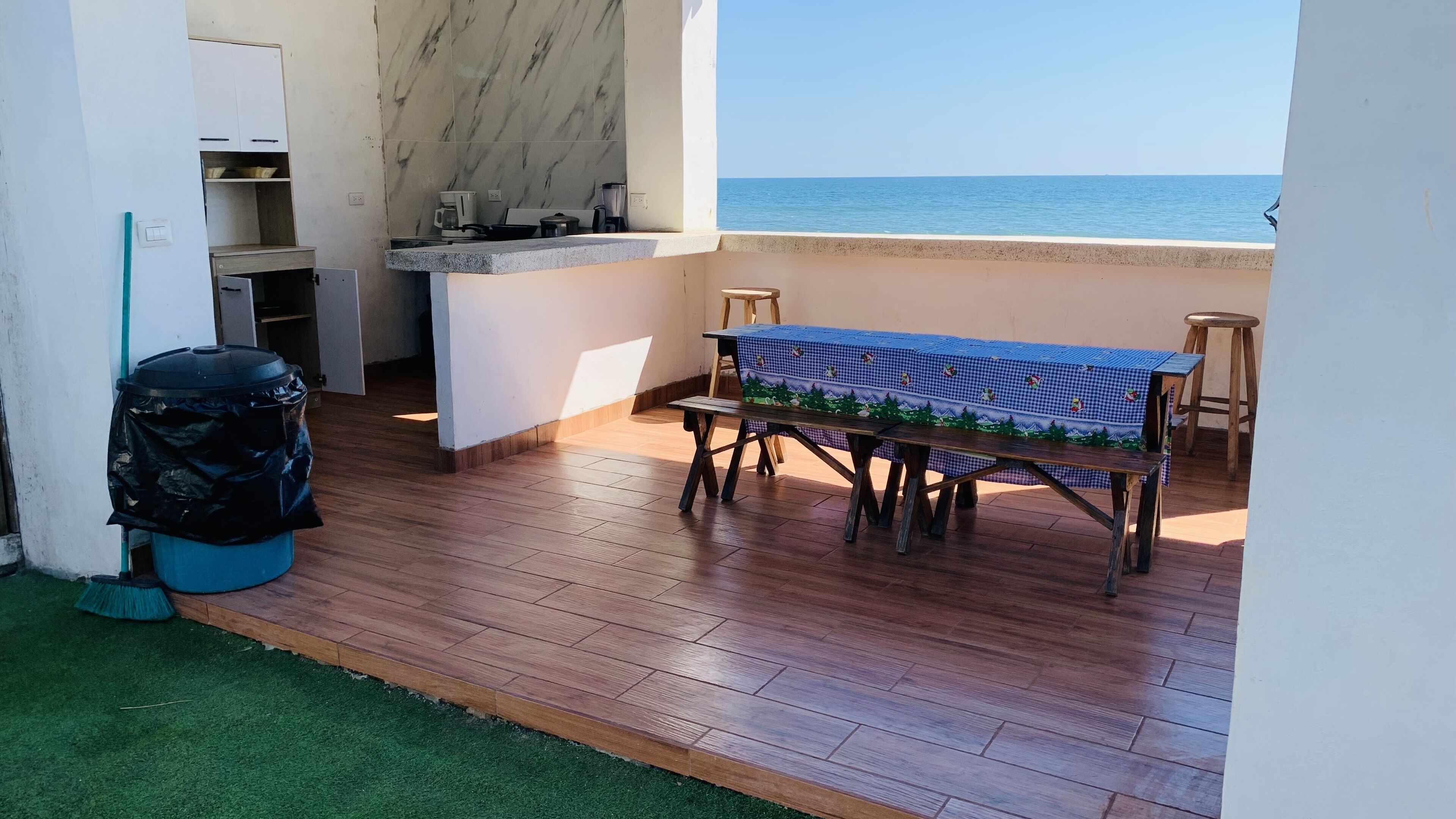 A balcony with a wooden floor, a table with a checkered tablecloth, and a view of the sea.