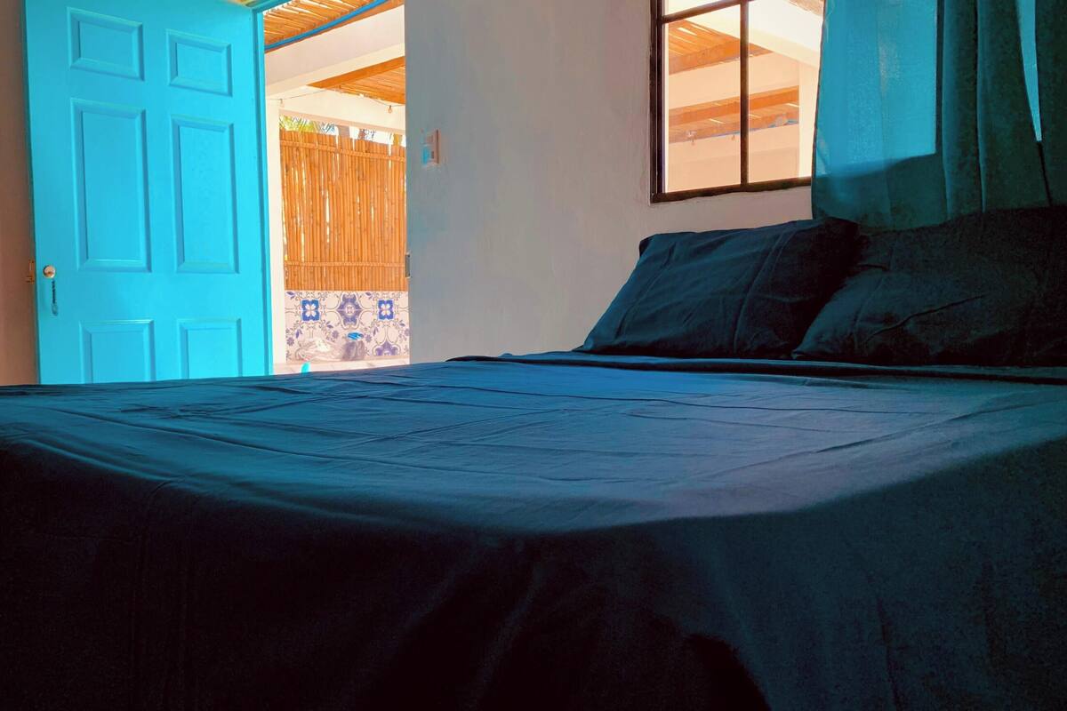 A bedroom with a bed, a blue door, and a window.