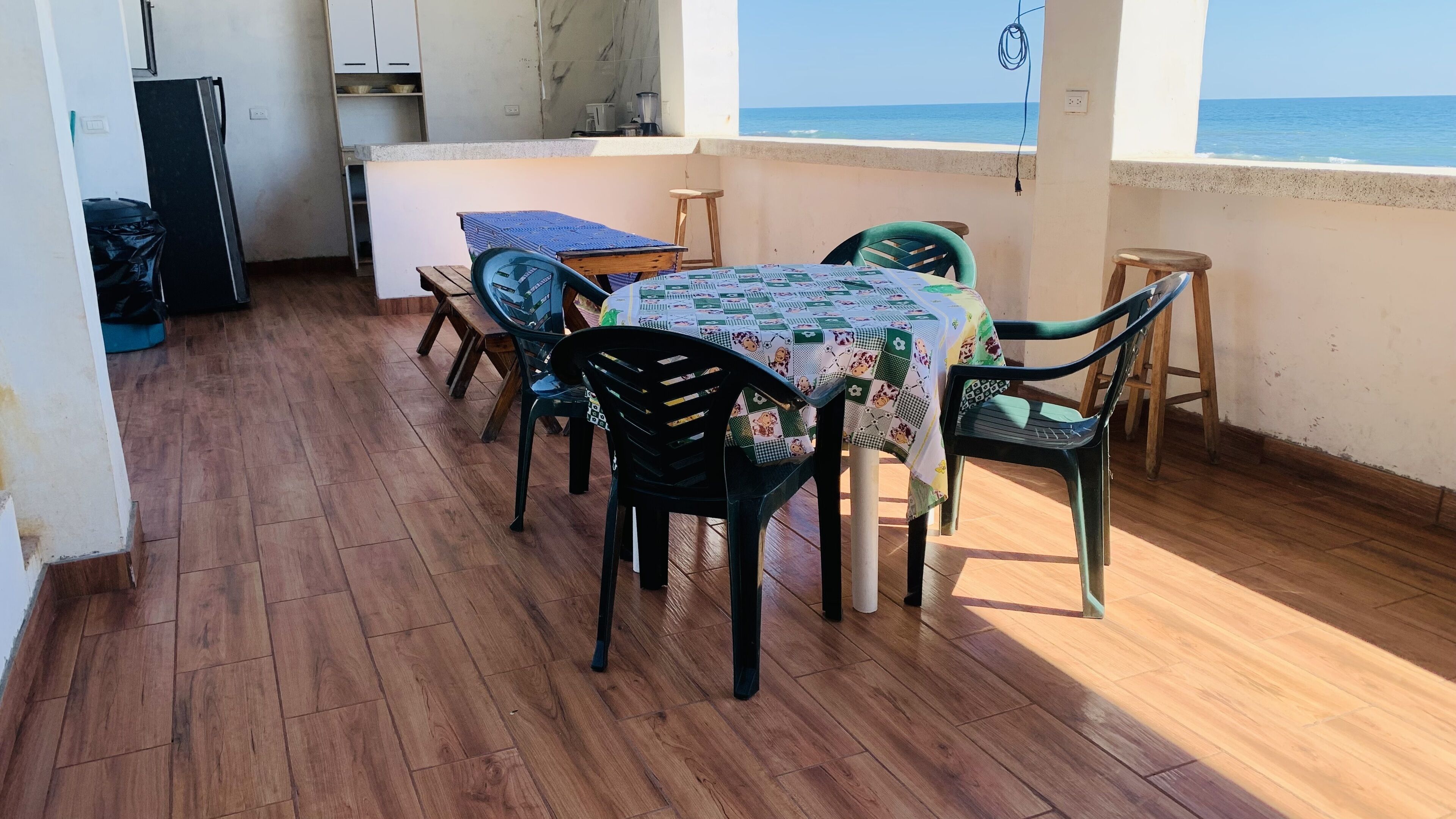 Un balcón con piso de madera, una mesa con mantel estampado y sillas.