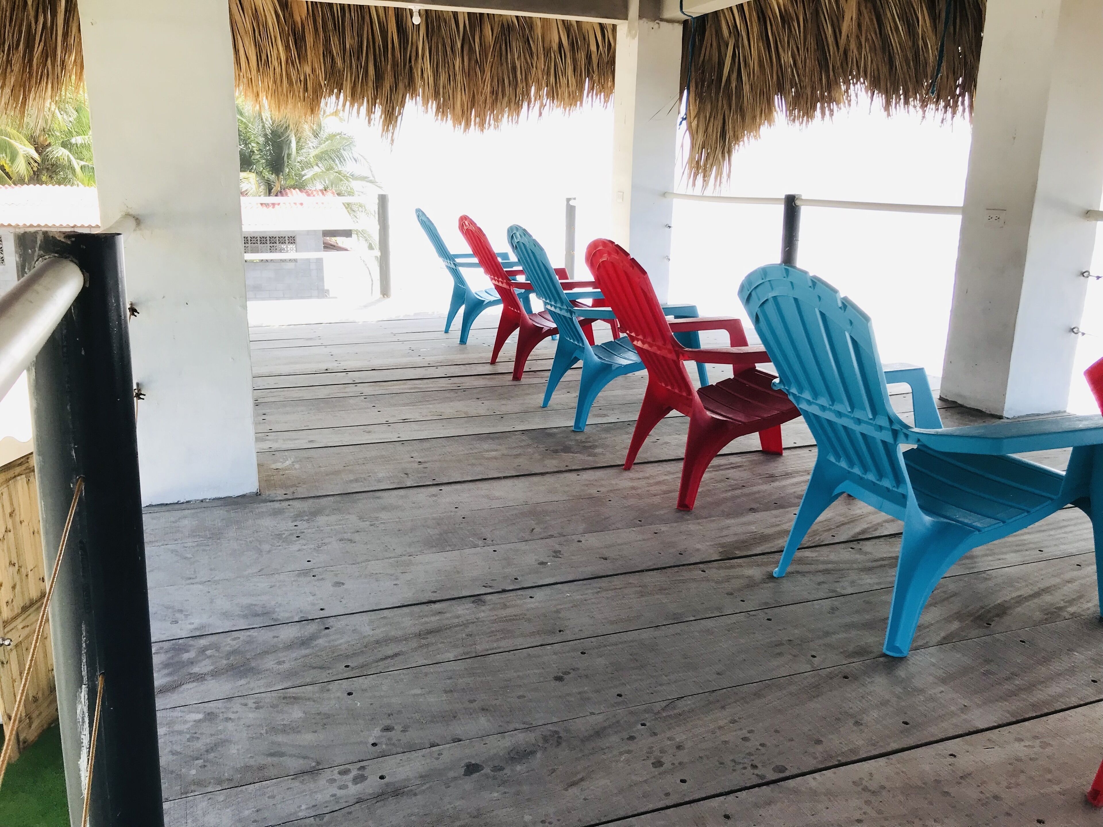 A covered outdoor seating area with rows of plastic chairs and a wooden deck.