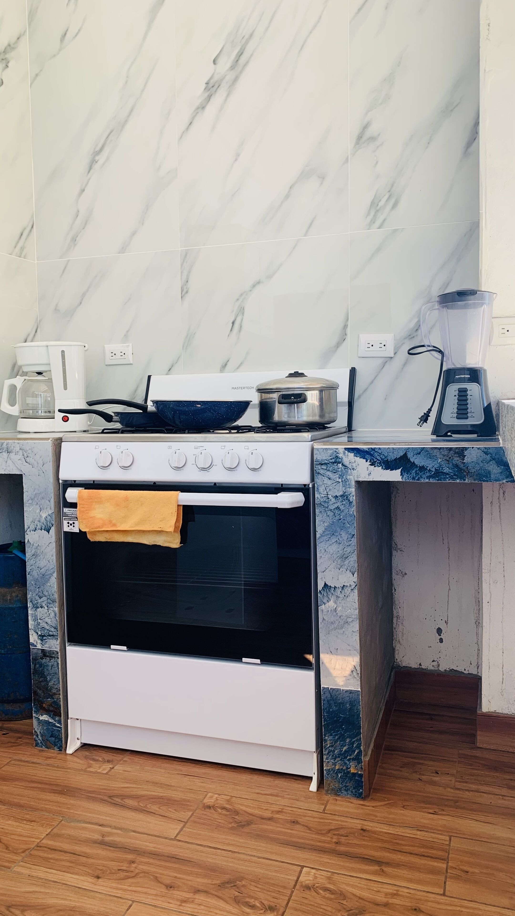 Een keuken met een wit fornuis, oven en een aanrecht met een koffiezetapparaat, een pan en een blender.