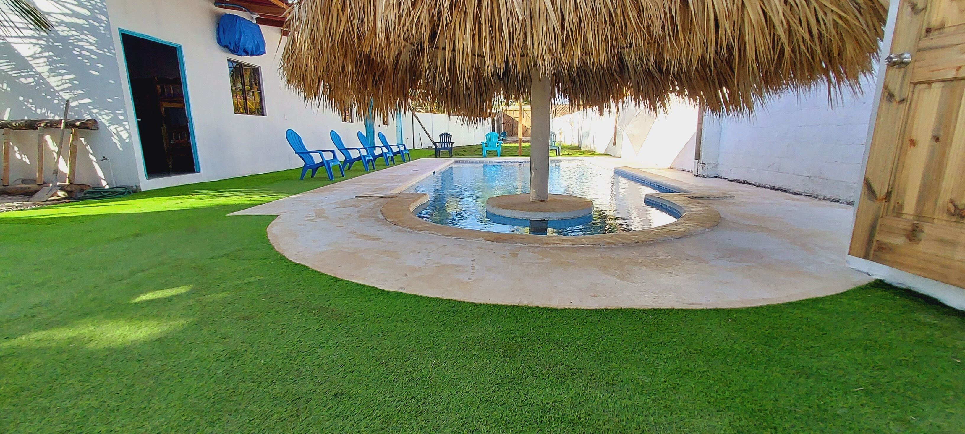 A circular pool with a central fountain, surrounded by a concrete deck and a grassy area.