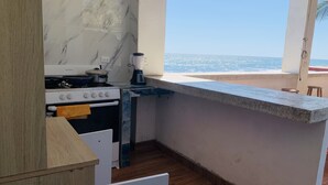 A compact kitchen with a stove, oven, and a blender on the counter, overlooking a beach. - Aqua Vista Beach House (Sonsonate)