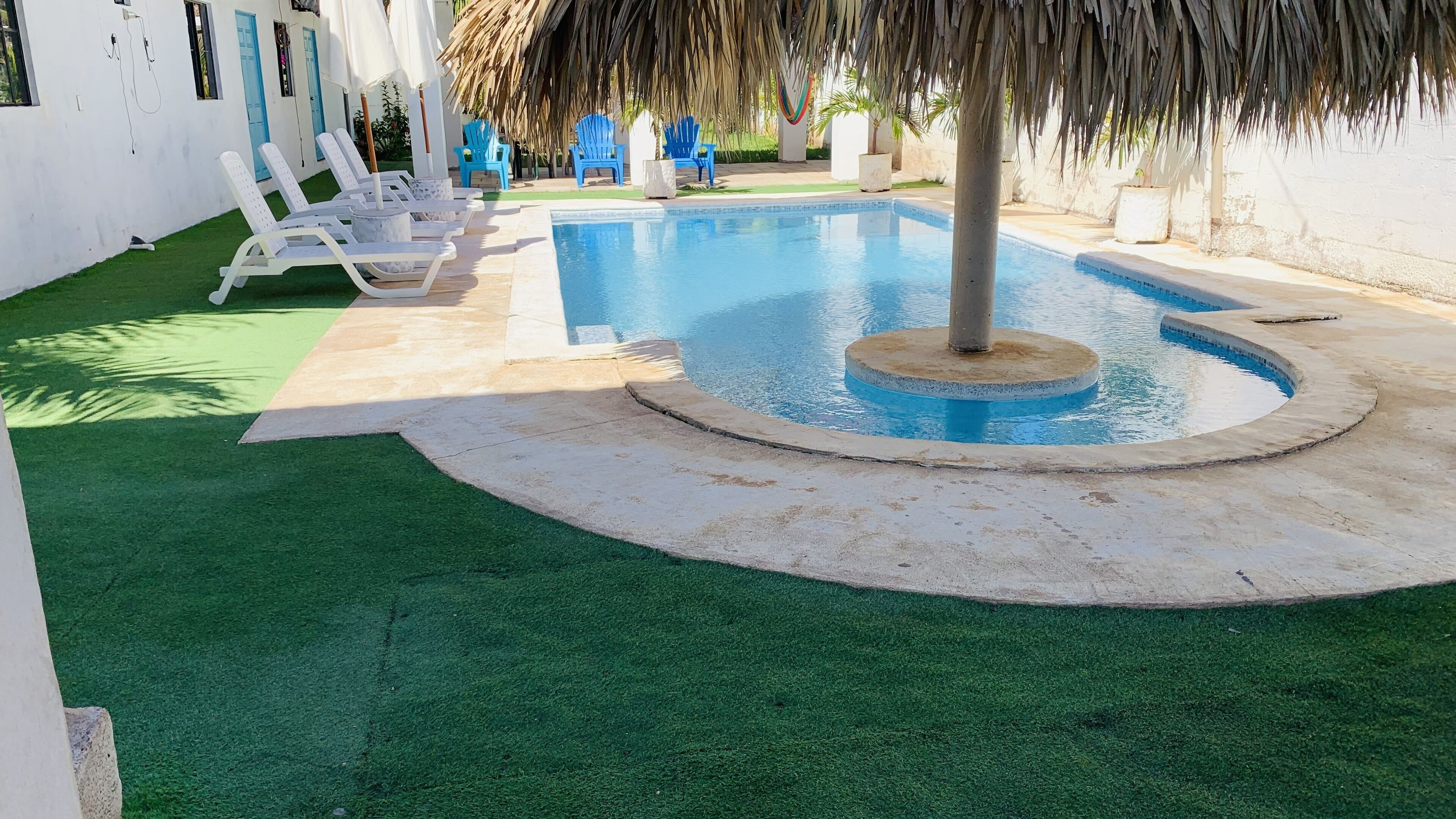 A swimming pool with a circular design, surrounded by artificial grass and blue chairs.