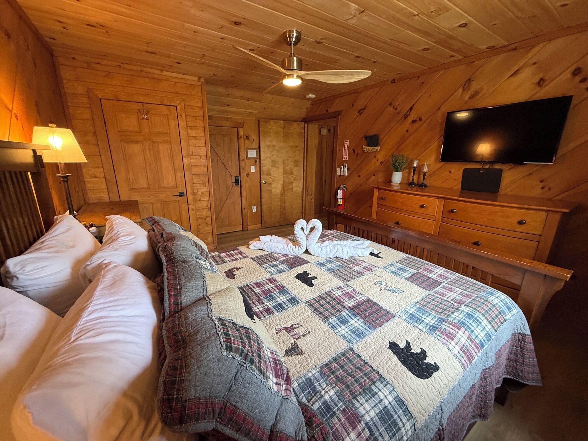 A wooden-paneled room with a bed, a television, and a dresser.