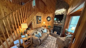 Ein gemütliches Blockhaus-Interieur mit einer Holztreppe, einem Kamin, einer Couch und einem Fernseher.
