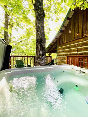 Un espace avec un jacuzzi, doté d’une terrasse en bois, entouré d’arbres et comprenant un coin salon abrité.